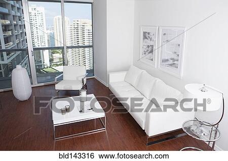 Stock Photograph - Sofa, coffee table and windows in modern apartment overlooking high rise buildings. Fotosearch