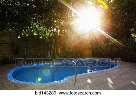 Stock Photo - Sunbeams over swimming pool in backyard. Fotosearch