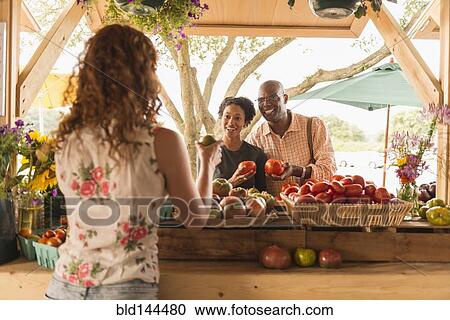 Stock Image - Vendor showing produce to couple at farmers market. Fotosearch