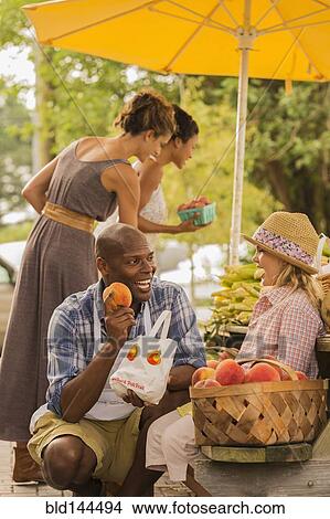 Picture - Vendor showing produce to girl at farmers market. Fotosearch