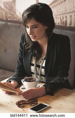 Stock Image - Woman reading with cup of coffee in cafe. Fotosearch