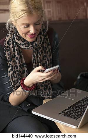 Stock Image - Woman using cell phone and laptop in cafe. Fotosearch