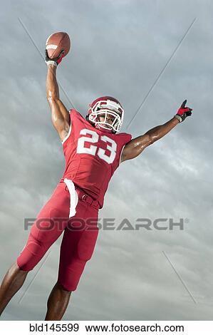 Stock Photo - African American football player with arms raised holding football. Fotosearch