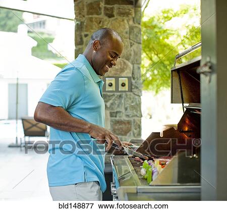 Stock Photo - African American man grilling food on barbecue. Fotosearch