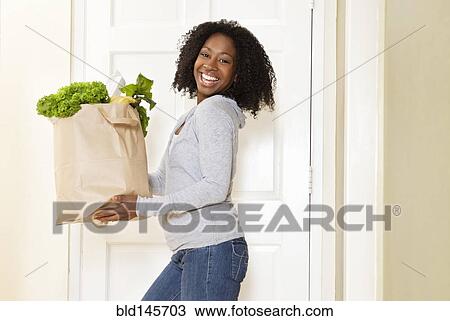 Stock Image - African American woman carrying bag of groceries. Fotosearch