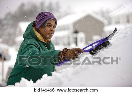 Stock Photograph - African American woman scraping snow from windshield. Fotosearch