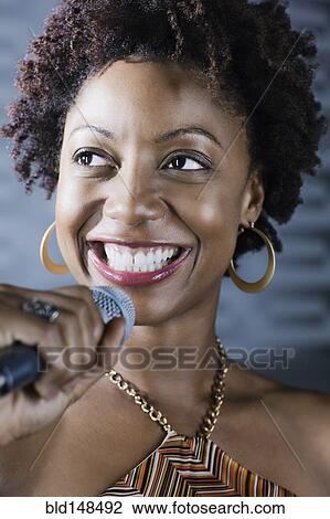 Stock Image - African American woman singing karaoke in nightclub. Fotosearch