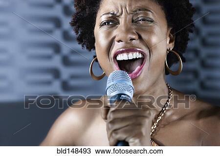 Stock Image - African American woman singing karaoke in nightclub. Fotosearch