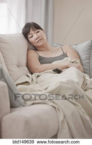 Stock Photo - Asian woman laying on sofa watching television. Fotosearch