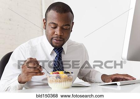 Black businessman eating breakfast at desk View Large Photo Image Stock Photo - Black businessman eating breakfast at desk. Fotosearch