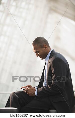 Stock Photo - Black businessman text messaging on cell phone. Fotosearch