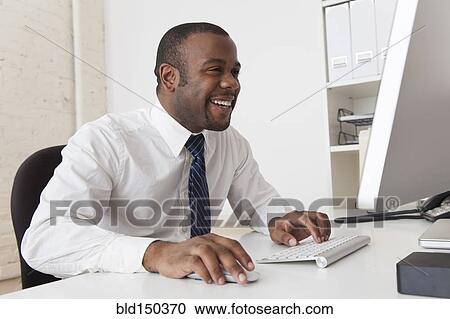 Stock Image - Black businessman using computer at desk. Fotosearch