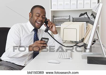 Stock Photo - Black businessman using two telephones at one time. Fotosearch