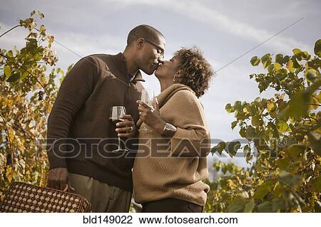 Stock Image - Black couple drinking wine in vineyard. Fotosearch