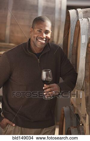 Picture - Black man drinking wine near wine barrel. Fotosearch