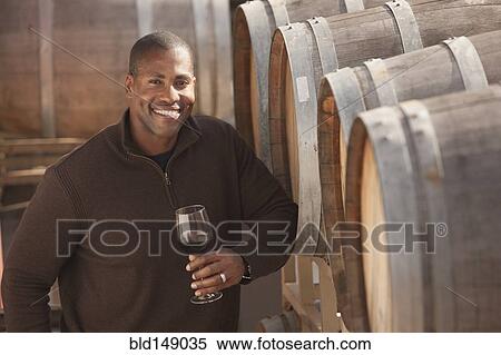Stock Photography - Black man drinking wine near wine barrel. Fotosearch