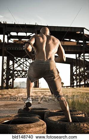 Stock Image - Black man running through tire obstacle course. Fotosearch