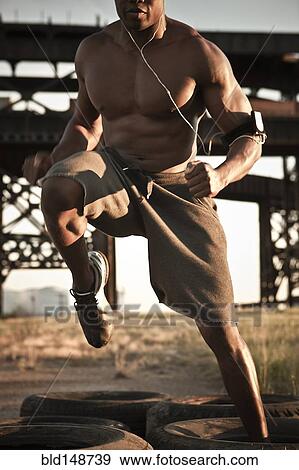 Stock Photo - Black man running through tire obstacle course. Fotosearch