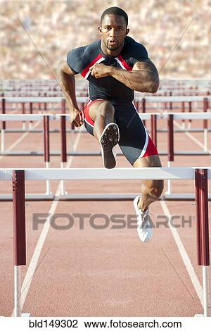 Stock Image - Black runner jumping hurdles in track race. Fotosearch