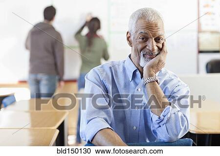 Stock Image - Black teacher sitting in classroom. Fotosearch