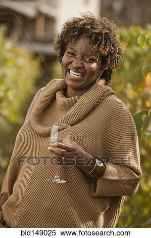 Stock Photography - Black woman drinking wine in vineyard. Fotosearch
