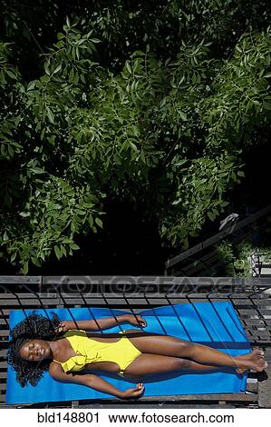 Stock Image - Black woman sunbathing on fire escape. Fotosearch