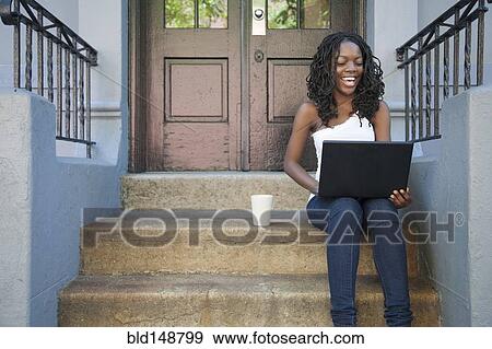 Stock Photo - Black woman using laptop on front stoop. Fotosearch