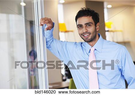 Businessman leaning against wall in office View Large Photo Image Stock Image - Businessman leaning against wall in office. Fotosearch