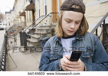 Stock Image - Caucasian boy text messaging on cell phone on sidewalk. Fotosearch