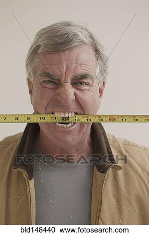 Stock Image - Caucasian carpenter biting measuring tape. Fotosearch