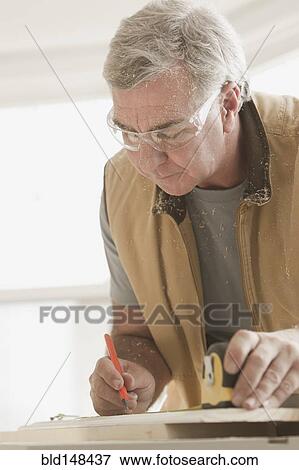 Stock Photo - Caucasian carpenter measuring lumber. Fotosearch