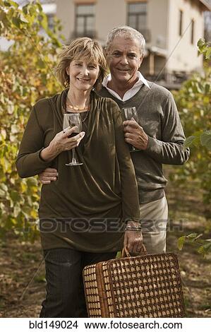Picture - Caucasian couple drinking wine in vineyard. Fotosearch