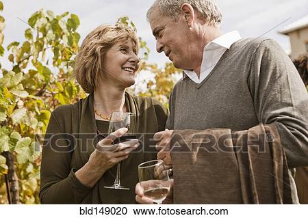 Stock Image - Caucasian couple drinking wine in vineyard. Fotosearch