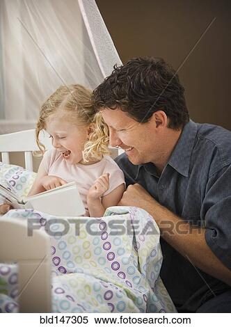 Stock Photography - Caucasian father reading book to daughter in bed. Fotosearch
