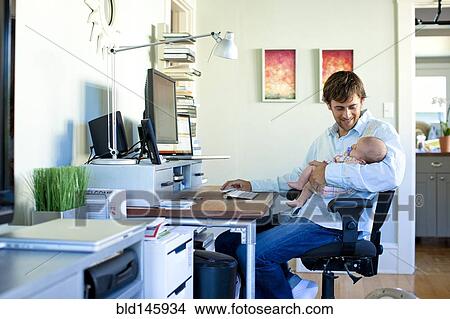Caucasian father working in home office and holding baby View Large Photo Image Picture - Caucasian father working in home office and holding baby. Fotosearch
