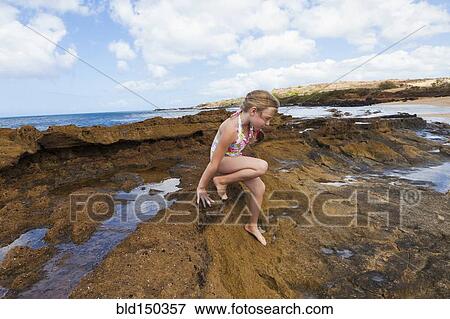 Stock Photo - Caucasian girl playing on rocks near ocean. Fotosearch