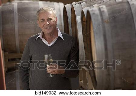 Stock Image - Caucasian man drinking wine near wine barrel. Fotosearch