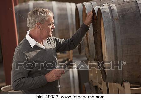 Stock Image - Caucasian man drinking wine near wine barrel. Fotosearch