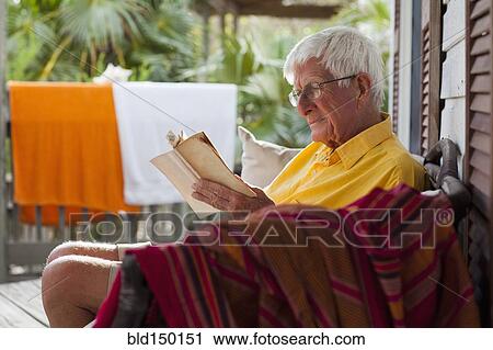 Stock Image - Caucasian man reading on porch. Fotosearch