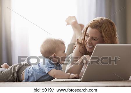 Stock Photo - Caucasian mother and son using laptop on floor. Fotosearch