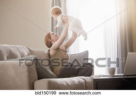 Stock Photo - Caucasian mother on sofa lifting son. Fotosearch