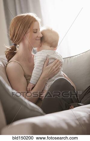 Stock Image - Caucasian mother sitting on sofa holding son. Fotosearch