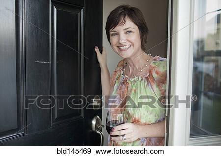 Stock Photo - Caucasian woman holding wine glass and opening door. Fotosearch