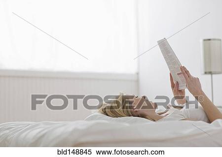 Stock Photography - Caucasian woman laying in bed reading paperwork. Fotosearch