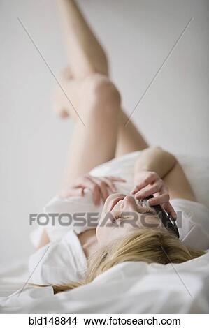 Picture - Caucasian woman laying in bed talking on cell phone. Fotosearch