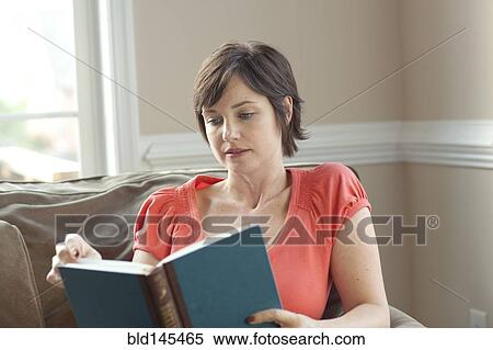 Stock Photography - Caucasian woman on sofa reading book. Fotosearch