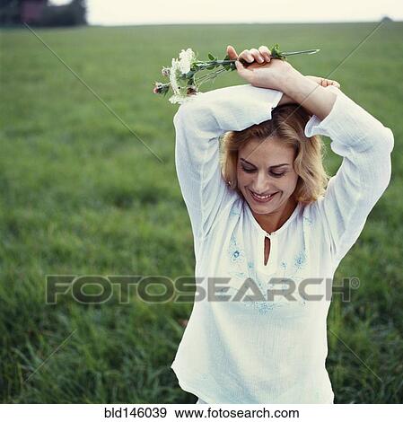 Stock Photo - Caucasian woman standing in green field with flowers. Fotosearch