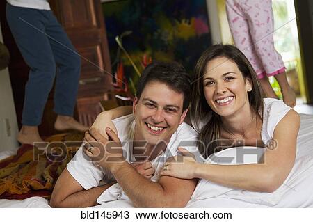 Stock Image - Children jumping on bed while parents smile. Fotosearch