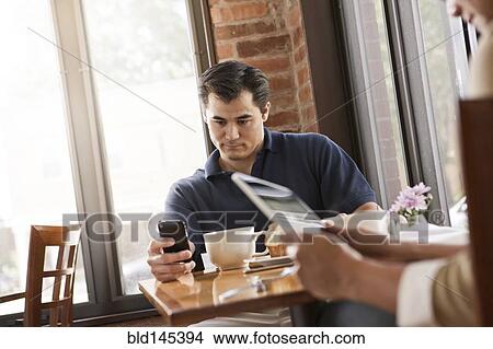 Picture - Chinese man using cell phone in cafe. Fotosearch