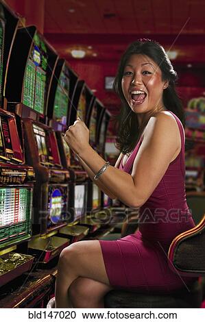 Stock Image - Chinese woman playing slot machines in casino. Fotosearch